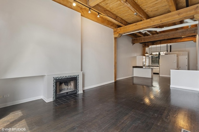 unfurnished living room featuring wooden ceiling, track lighting, dark wood-style flooring, beam ceiling, and a tile fireplace