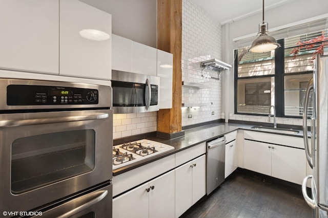 kitchen with appliances with stainless steel finishes, a sink, dark countertops, white cabinets, and decorative backsplash