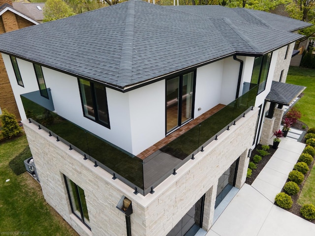 view of side of home featuring stucco siding, stone siding, and roof with shingles