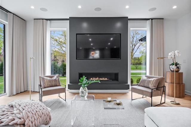 sitting room with recessed lighting, wood finished floors, and a warm lit fireplace