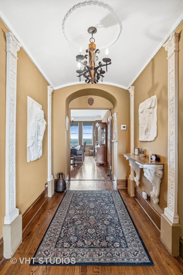 foyer entrance featuring arched walkways, a chandelier, decorative columns, wood finished floors, and ornamental molding