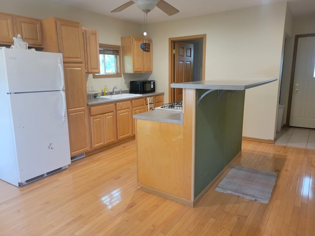 kitchen featuring freestanding refrigerator, black microwave, a sink, light wood-style floors, and ceiling fan