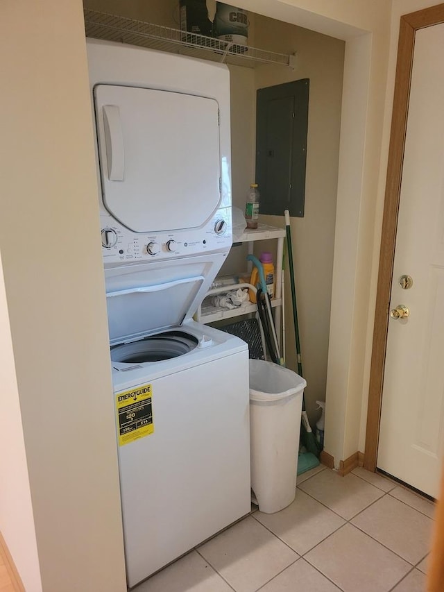 laundry area featuring estacked washer and dryer, electric panel, light tile patterned floors, and baseboards