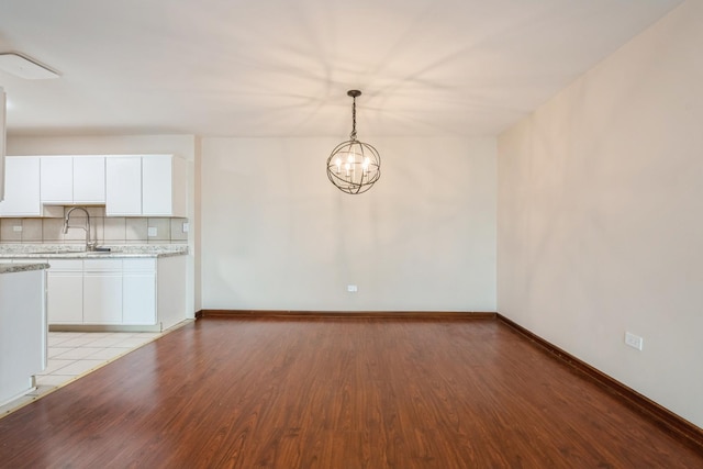 unfurnished dining area featuring light wood-type flooring, a sink, a chandelier, and baseboards
