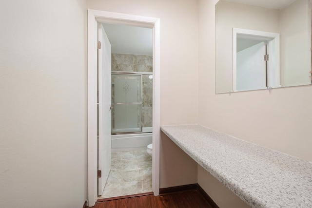 bathroom with toilet, wood finished floors, and enclosed tub / shower combo