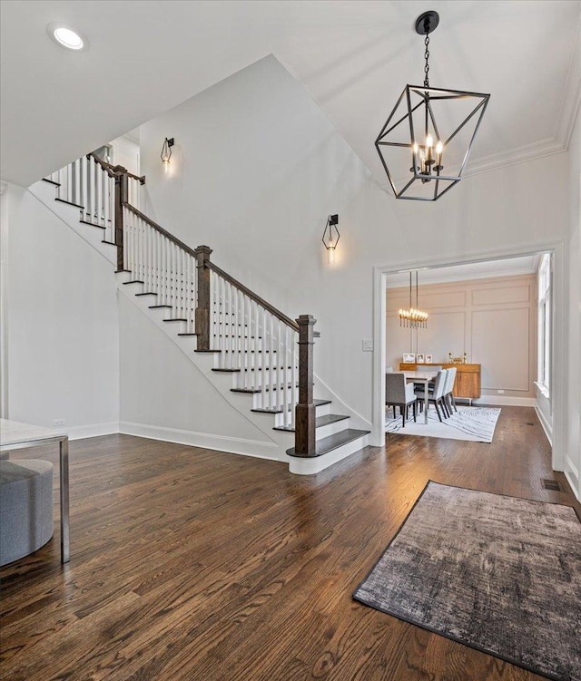 entrance foyer with a chandelier, stairs, wood finished floors, a high ceiling, and crown molding