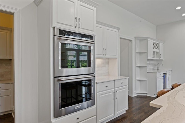 kitchen featuring stainless steel double oven, white cabinets, dark wood-style floors, decorative backsplash, and recessed lighting