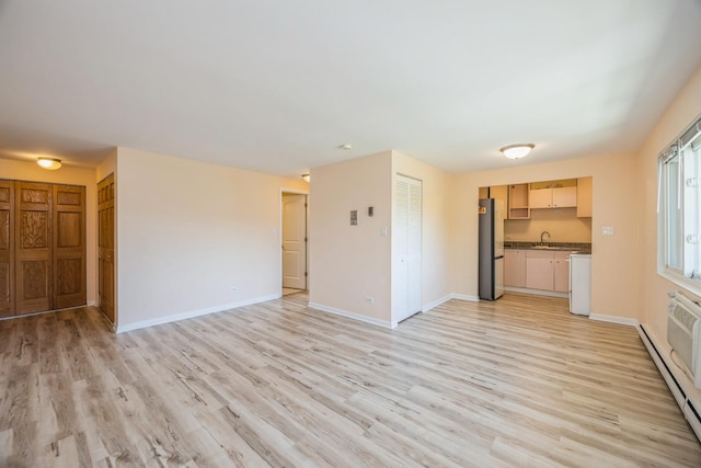 unfurnished living room featuring a sink, baseboard heating, light wood-style floors, and baseboards