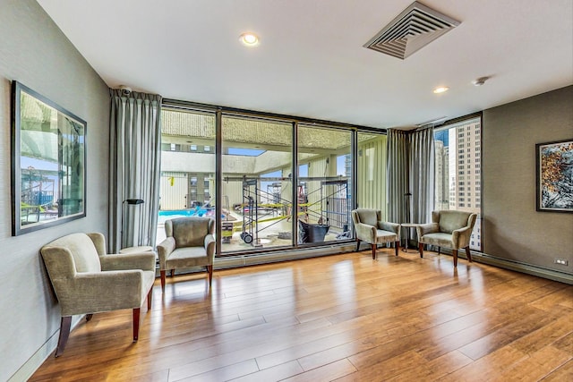 living area with plenty of natural light, wood finished floors, a baseboard radiator, a wall of windows, and recessed lighting