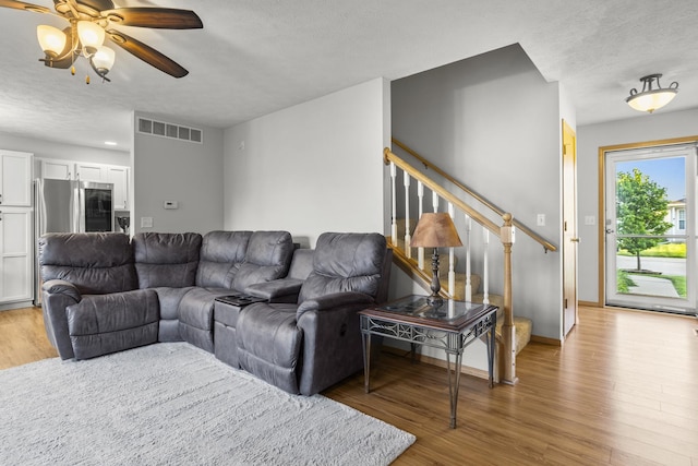 8 Harrison Ct, Bloomington, IL 61704 - living room featuring stairs, light wood-type flooring, a ceiling fan, a textured ceiling, and baseboards