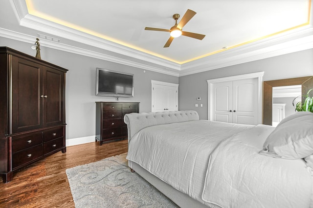 bedroom featuring a raised ceiling, crown molding, dark wood-type flooring, a ceiling fan, and baseboards