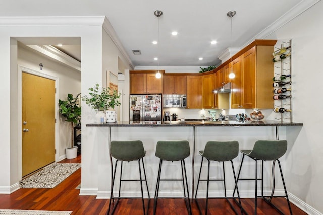 kitchen featuring stainless steel appliances, a kitchen breakfast bar, dark stone counters, under cabinet range hood, and crown molding