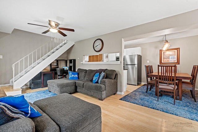 living room featuring stairway, light wood-style floors, ceiling fan, and baseboards