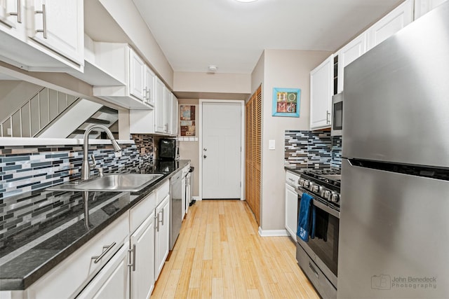 kitchen with appliances with stainless steel finishes, a sink, white cabinets, tasteful backsplash, and light wood-style flooring