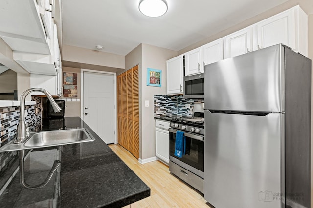 kitchen featuring appliances with stainless steel finishes, white cabinets, decorative backsplash, light wood-style floors, and dark stone counters