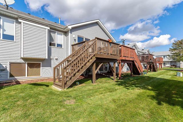 back of property featuring stairway, a deck, and a lawn