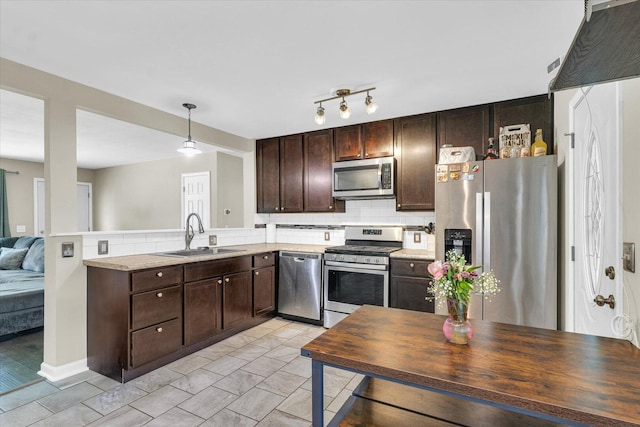 kitchen with appliances with stainless steel finishes, a sink, dark brown cabinetry, decorative backsplash, and light countertops