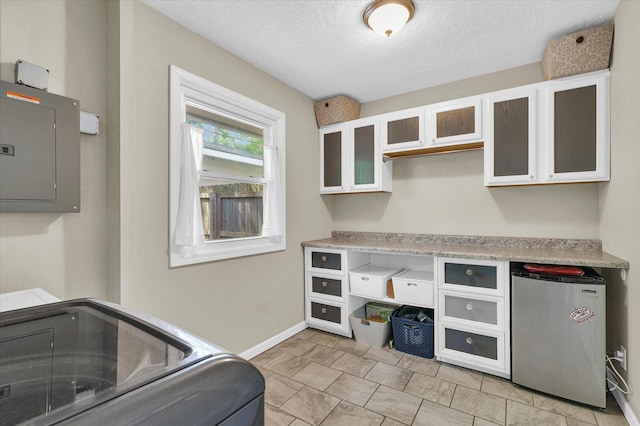 laundry area with electric panel, baseboards, and a textured ceiling