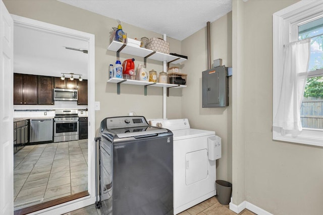 clothes washing area featuring electric panel, washer and dryer, light tile patterned floors, and baseboards