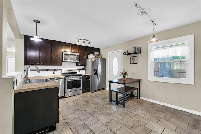 kitchen featuring stainless steel appliances, a sink, rail lighting, backsplash, and dark brown cabinetry