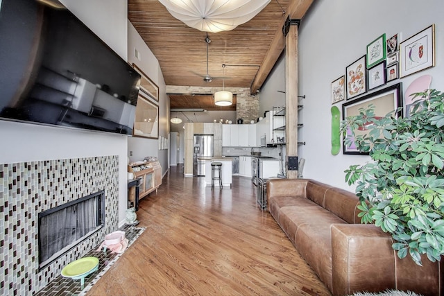 living room featuring a towering ceiling, wooden ceiling, light wood finished floors, and a tile fireplace