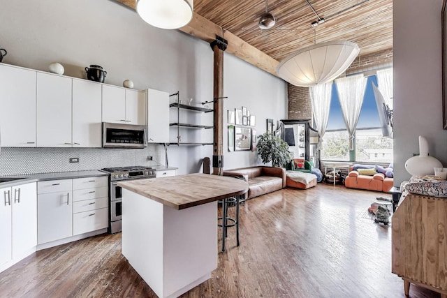 kitchen with appliances with stainless steel finishes, wooden counters, a towering ceiling, open floor plan, and wood finished floors
