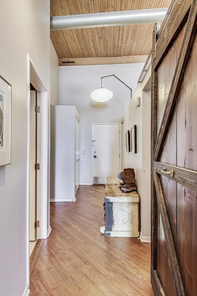 corridor featuring a barn door, light wood-type flooring, beam ceiling, wood ceiling, and a high ceiling