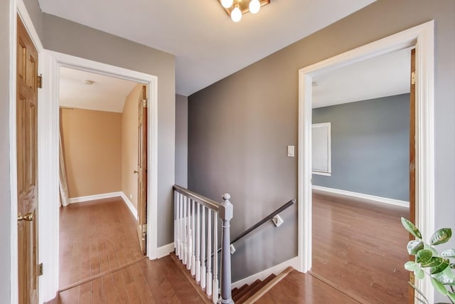 corridor with an upstairs landing, wood finished floors, and baseboards