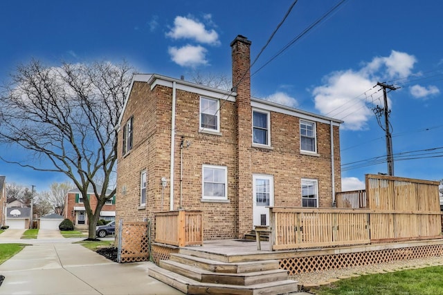 back of property featuring brick siding, a wooden deck, and a chimney
