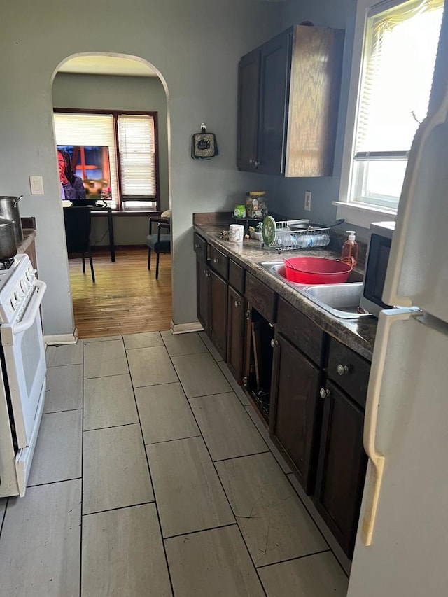 14027 S Mackinaw Ave, Burnham, IL 60633 - kitchen with white appliances, arched walkways, dark countertops, light tile patterned floors, and baseboards