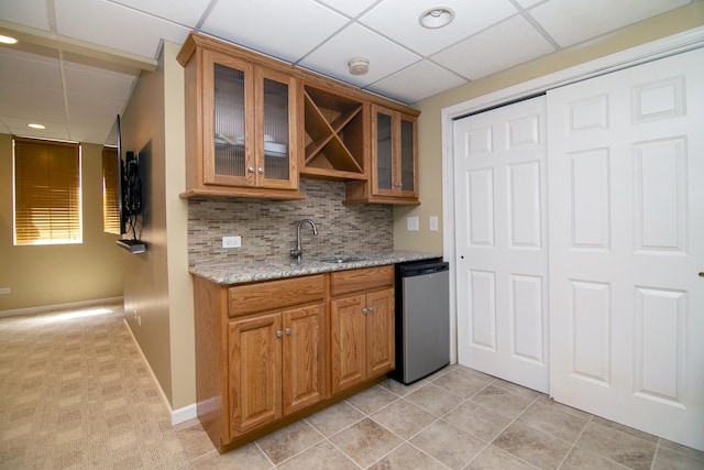 kitchen with dishwashing machine, a sink, brown cabinetry, decorative backsplash, and a drop ceiling