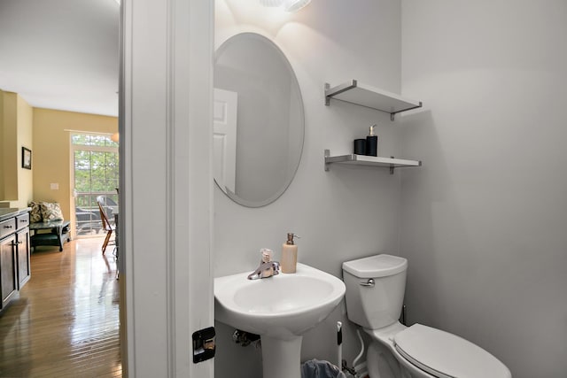 half bathroom with toilet, wood finished floors, and a sink