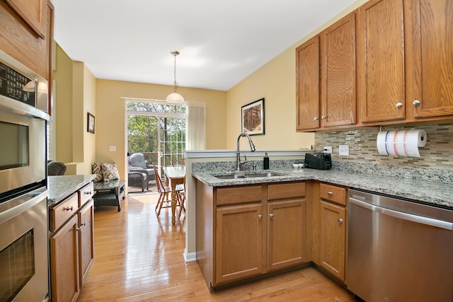 kitchen with stainless steel appliances, a sink, a peninsula, light wood-style floors, and backsplash