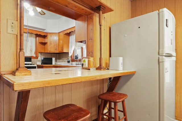 3132 Oak Park Ave, Berwyn, IL 60402 - kitchen featuring white appliances, tile counters, a peninsula, wood walls, and ceiling fan