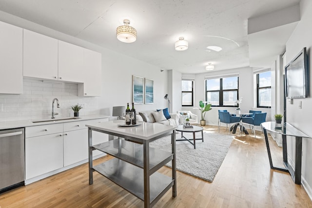 kitchen featuring a sink, stainless steel dishwasher, backsplash, light wood-style flooring, and white cabinets
