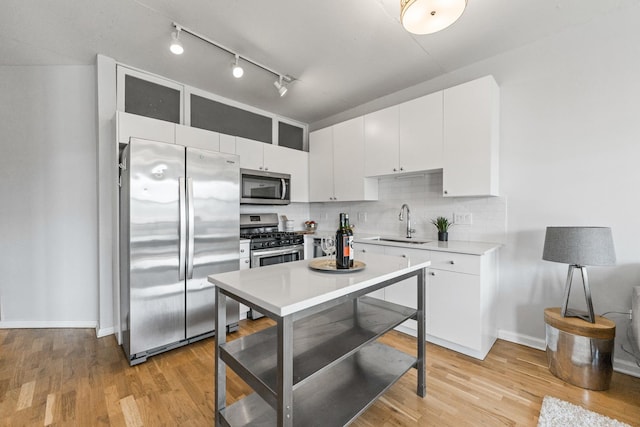 kitchen with appliances with stainless steel finishes, a sink, tasteful backsplash, and white cabinets