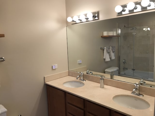 full bath with toilet, double vanity, and combined bath / shower with glass door