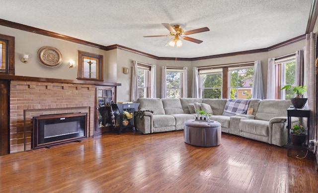 living area with healthy amount of natural light, a ceiling fan, a textured ceiling, wood finished floors, and a brick fireplace