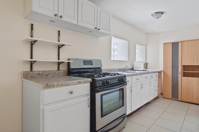 kitchen featuring stainless steel gas range oven, light countertops, white cabinets, open shelves, and light tile patterned flooring