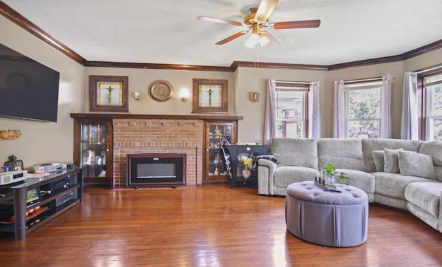 living area featuring a textured ceiling, ceiling fan, wood finished floors, a fireplace, and crown molding