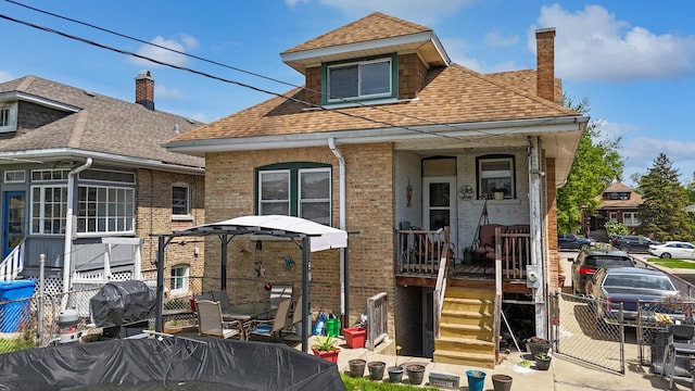 view of front of house with fence, brick siding, a chimney, covered porch, and a shingled roof