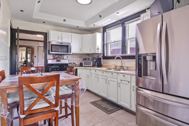 kitchen with stainless steel appliances, a sink, white cabinetry, backsplash, and light tile patterned floors
