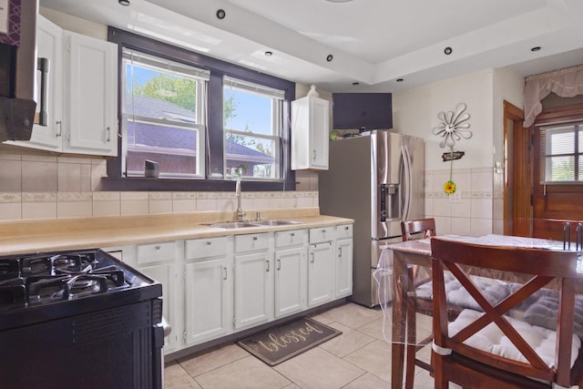 kitchen with stainless steel refrigerator with ice dispenser, black range with gas stovetop, a sink, light tile patterned flooring, and white cabinetry