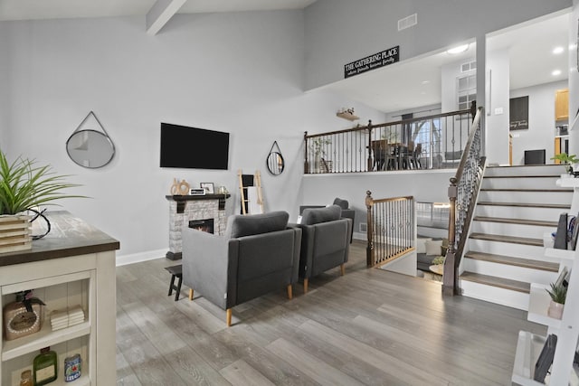 living area featuring wood finished floors, stairs, a stone fireplace, beamed ceiling, and baseboards