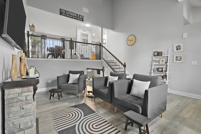 living area featuring a towering ceiling, wood finished floors, baseboards, and stairs
