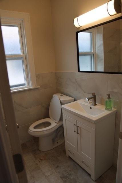 half bathroom with tile walls, toilet, vanity, and a wainscoted wall