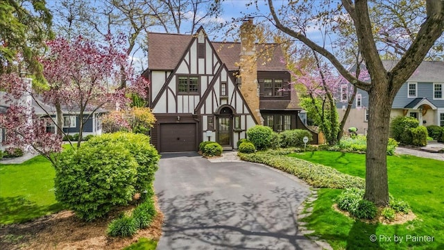 705 Hunter Rd, Glenview, IL 60025 - tudor house with an attached garage, asphalt driveway, stucco siding, a chimney, and a shingled roof