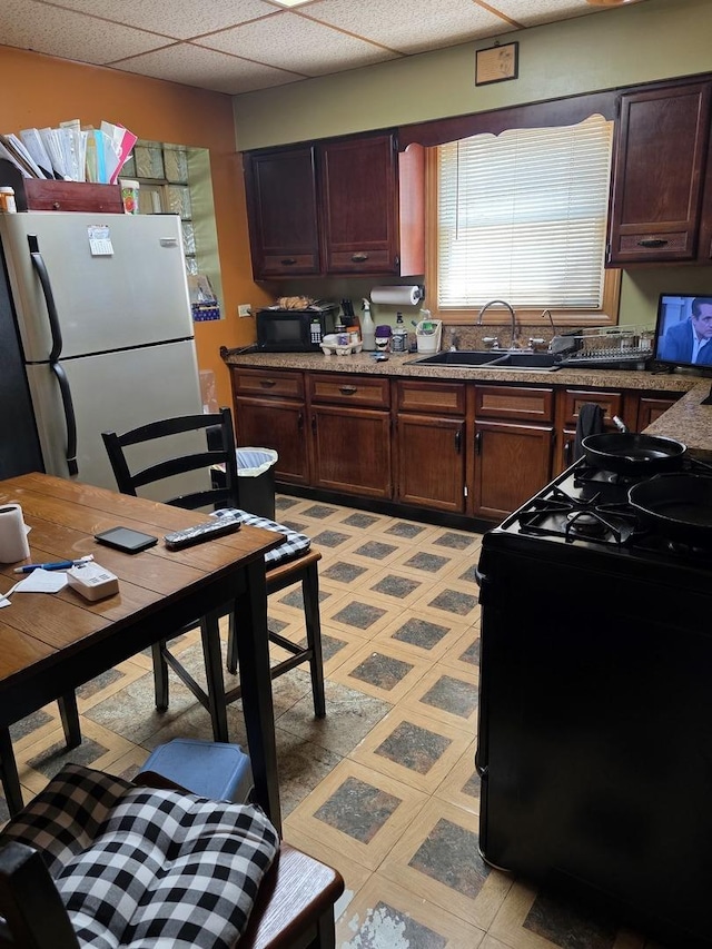 kitchen featuring black appliances, a sink, light floors, a paneled ceiling, and dark brown cabinets
