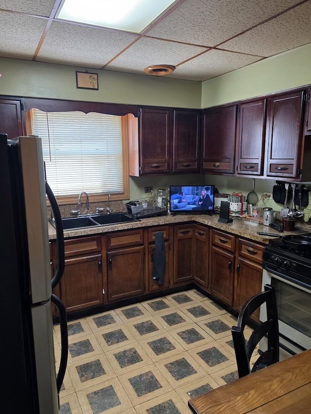 kitchen with freestanding refrigerator, a paneled ceiling, gas range, a sink, and dark brown cabinets