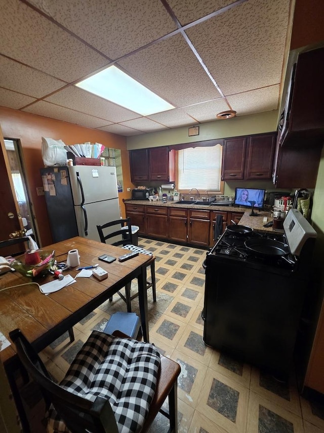 kitchen with freestanding refrigerator, range with gas stovetop, a drop ceiling, a sink, and light floors